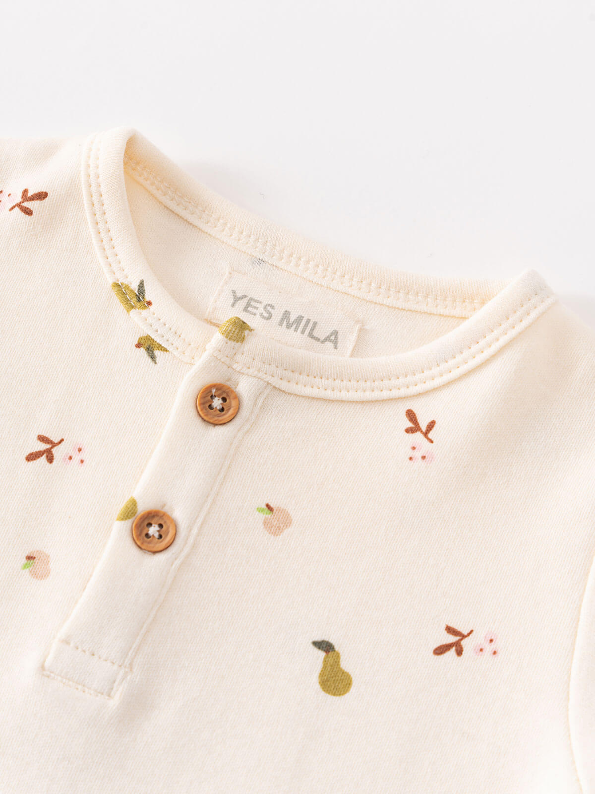 Close-up of cream-colored baby bodysuit with fruit pattern and wooden buttons Henley Short Sleeve Bodysuit - Autumn Harvest Ecru Baby girl