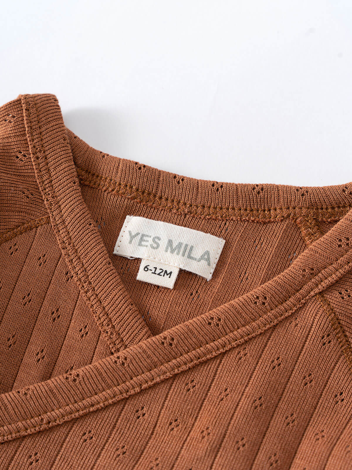 Close-up of a rust-colored knitted garment with white label showing size Pointelle Crossover Bodysuit - Russet Baby boy