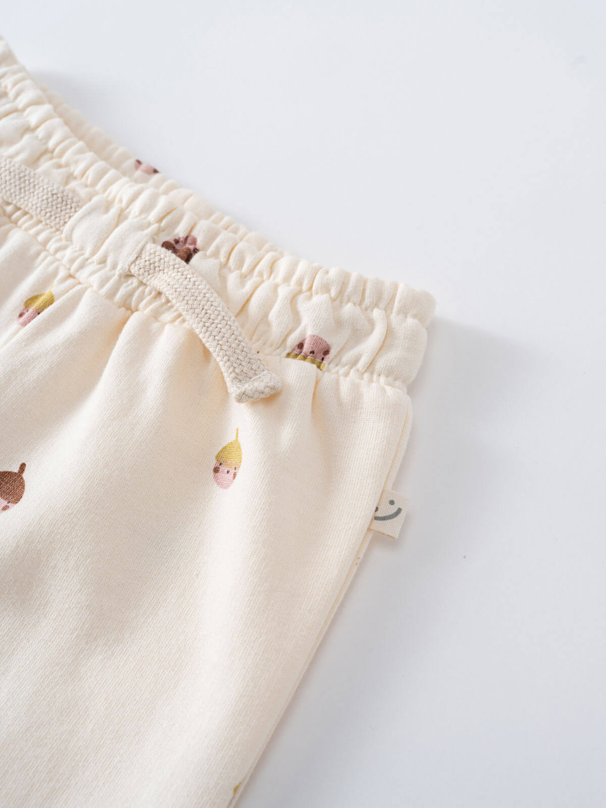 Close-up of cream-colored sweatpants waistband with small printed faces pattern Printed Sweatpants - Little Acorn Ecru Baby girl