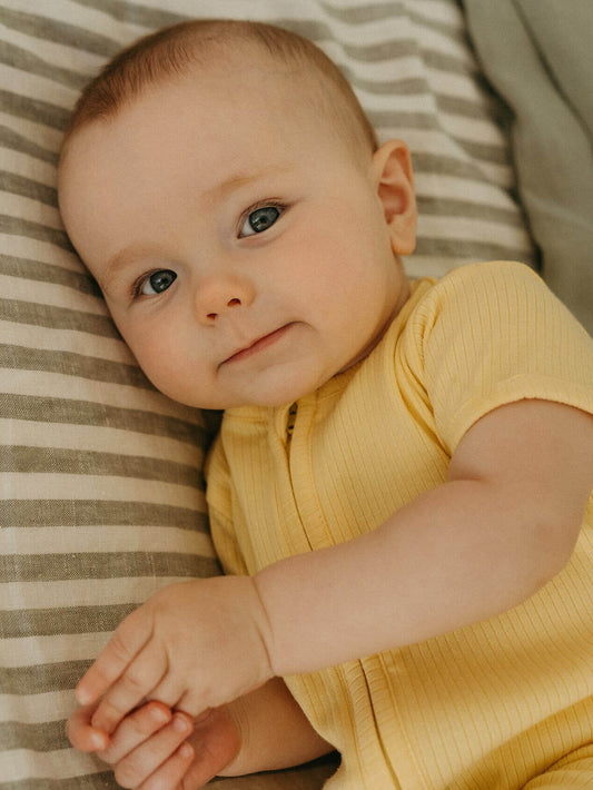 Baby in a yellow outfit lying on a striped surface