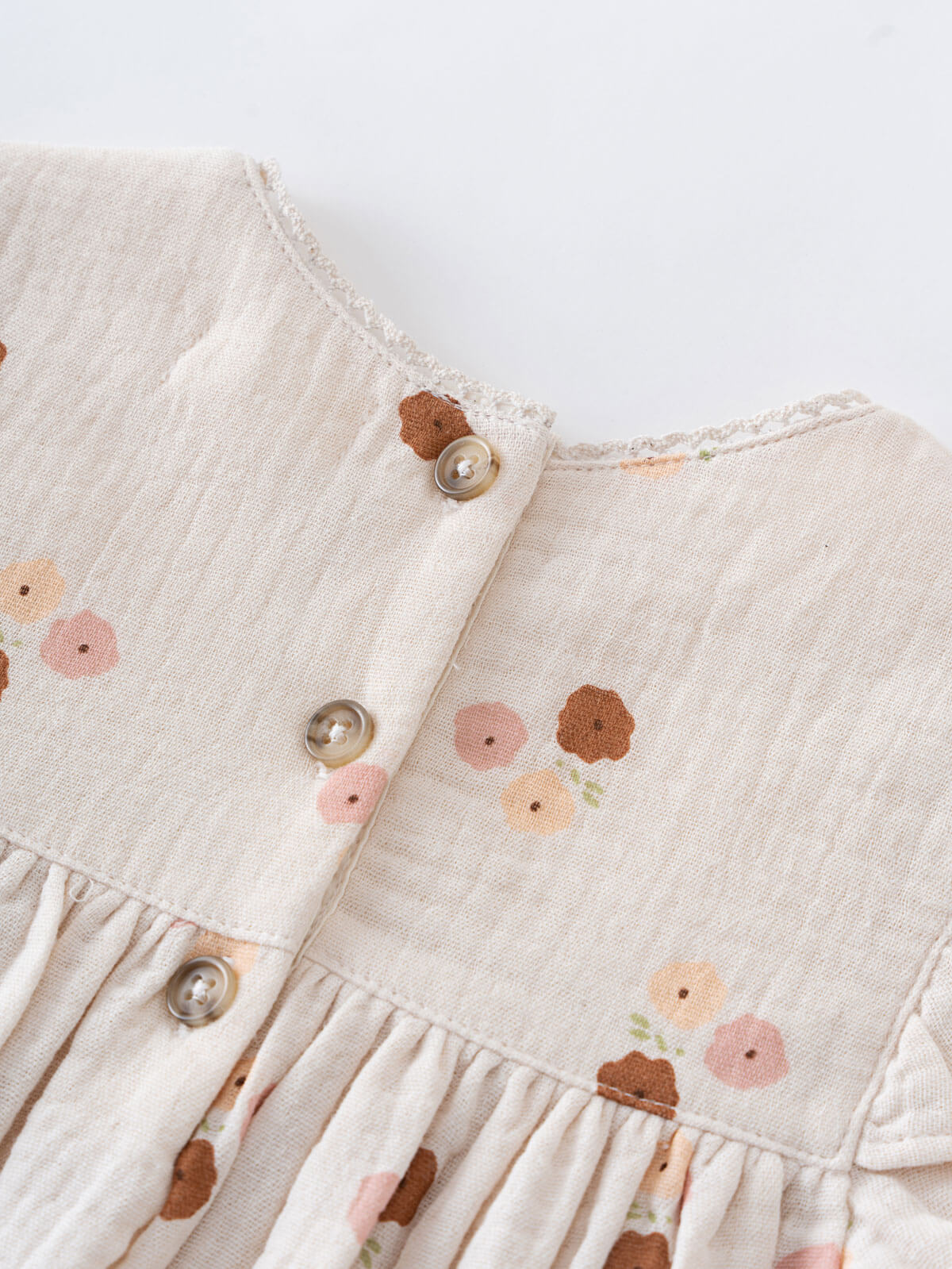 Close-up of a baby dress with floral patterns and buttons on a light background