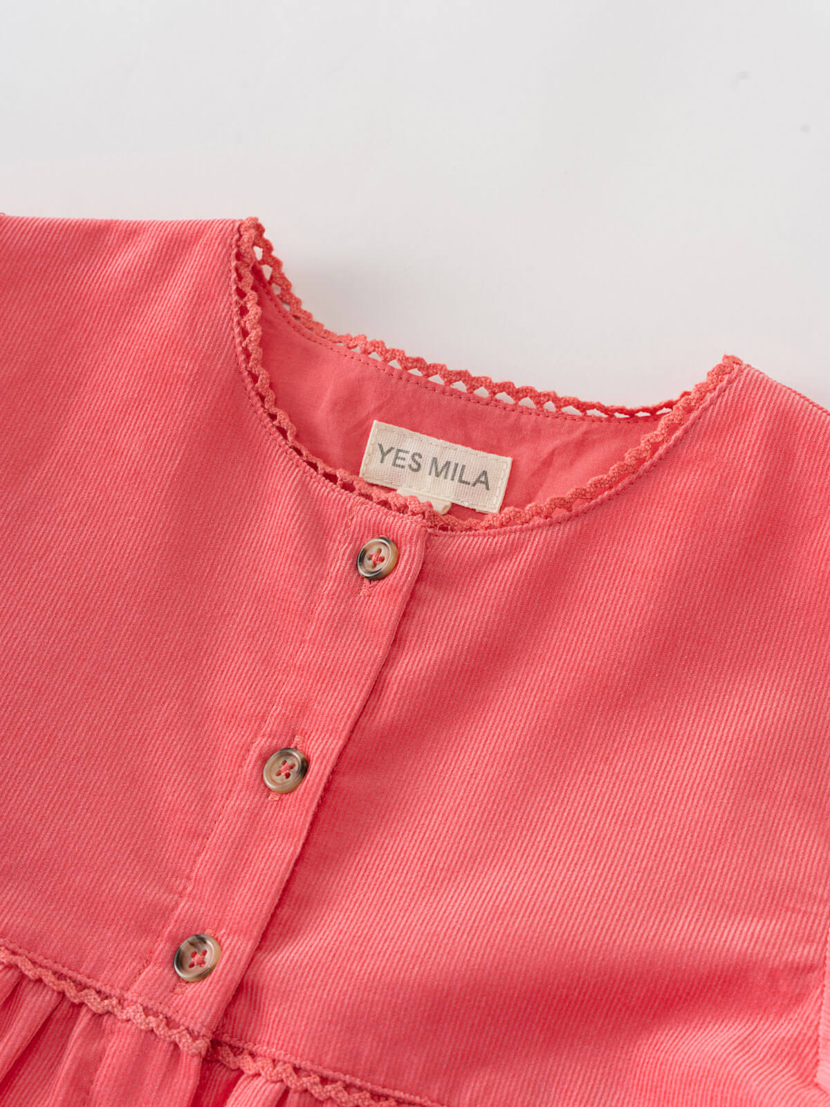 Close-up of a coral pink dress with 'YES MILA' label on a light gray background