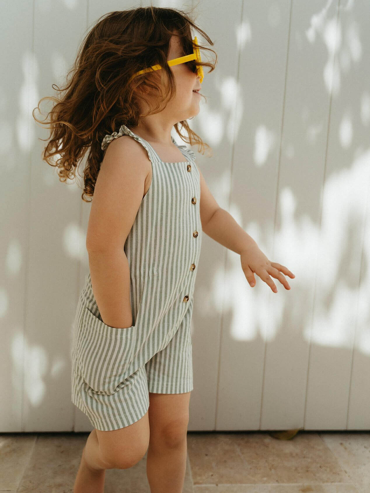 Young girl wearing a striped playsuit and yellow sunglasses against a white wall Ellie Playsuit - Mint Stripe Girls
