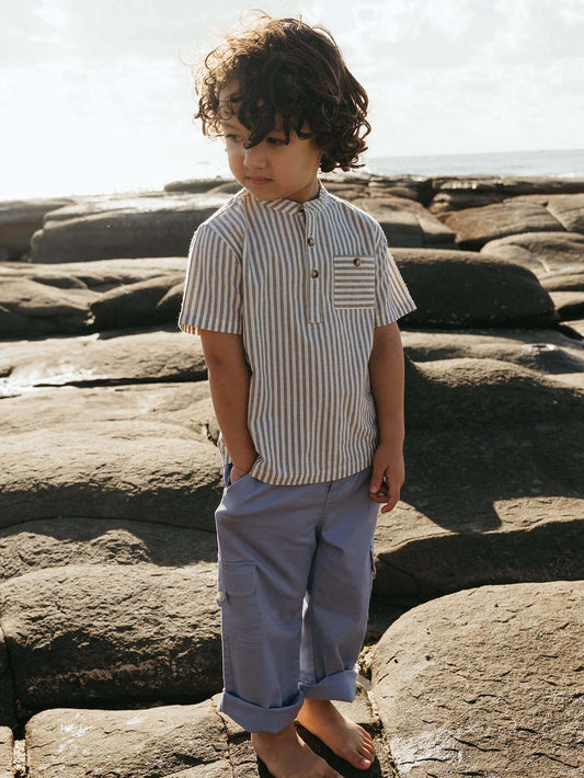 Child wearing a striped shirt and light pants standing on rocks with a natural background