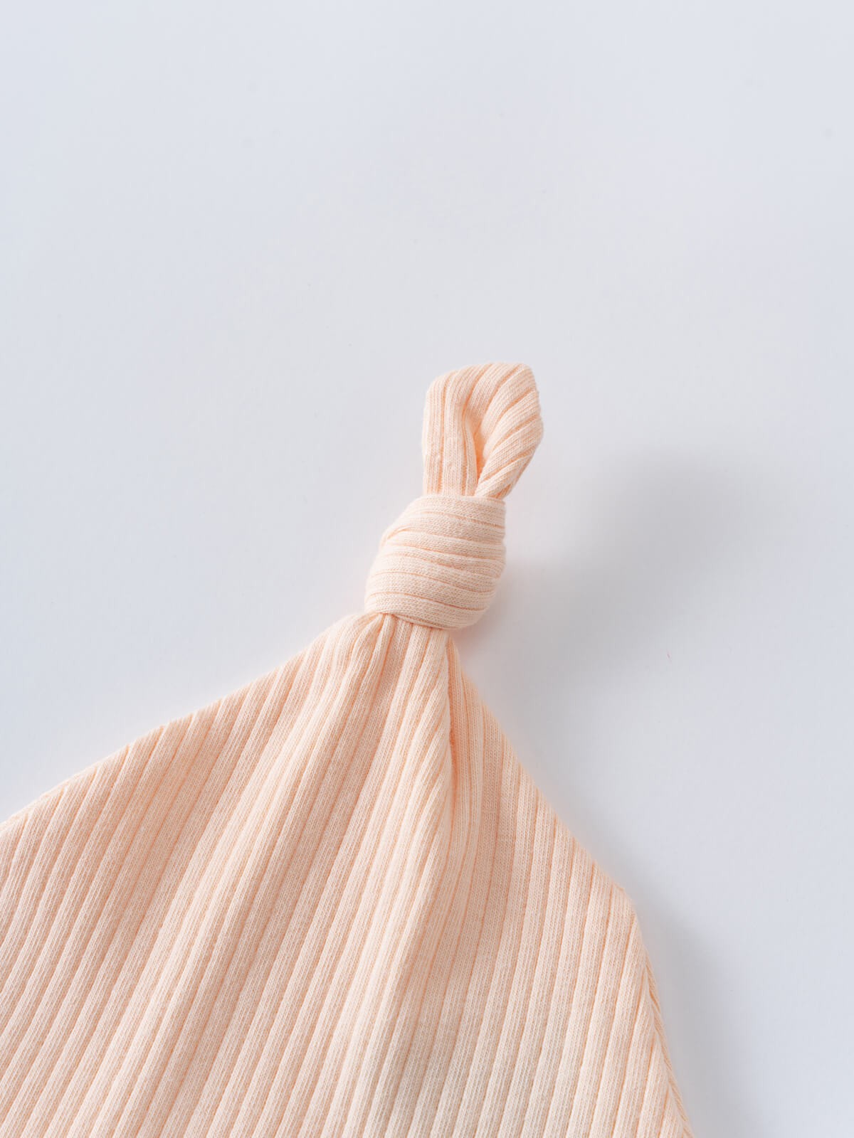 Close-up of a peach ribbed fabric baby hat with knotted top Jade Knot Hat - Apricot Baby girl