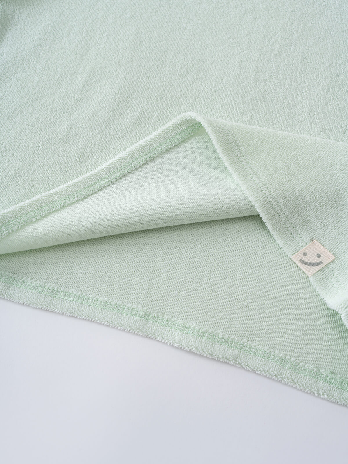 Close-up of folded mint green terry cloth fabric with white trim and small label Lara Towelling Tee Shirt - Mint Girls