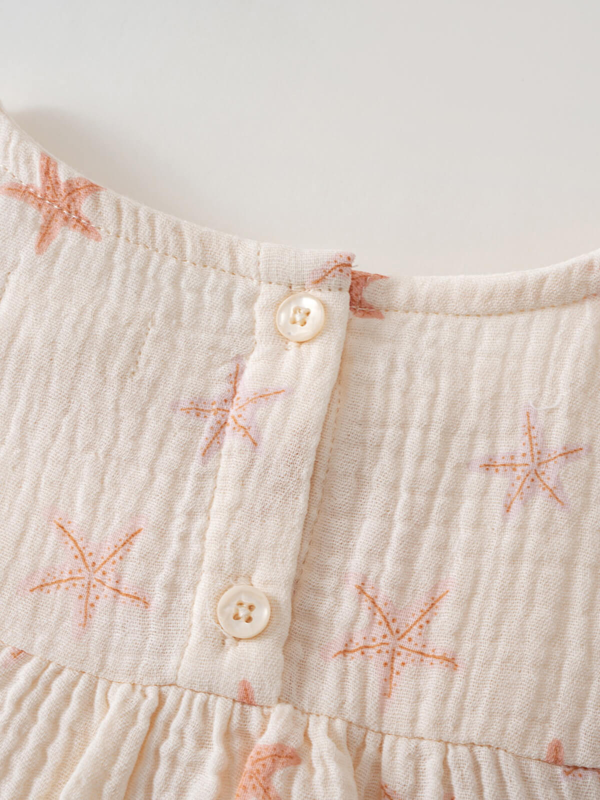 Close-up of cream fabric with orange starfish embroidery and button placket Luna Top - Starfish Girls