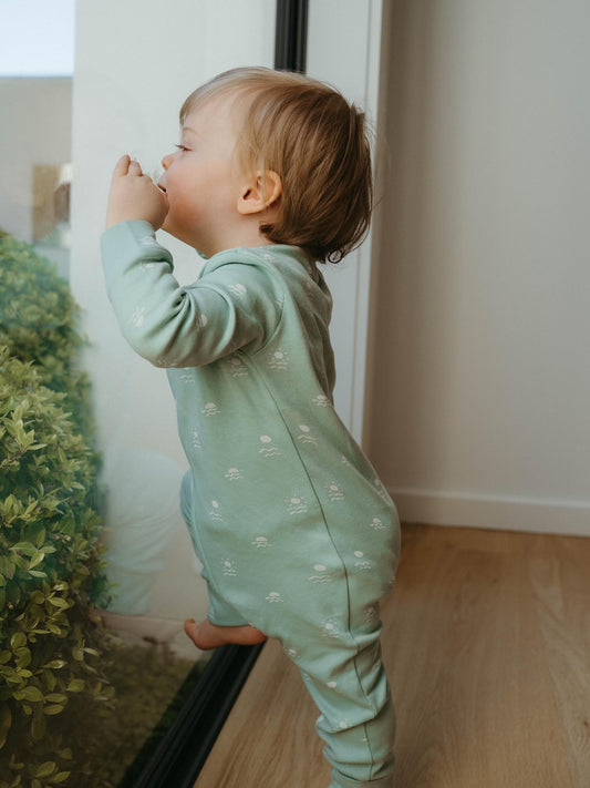 Child in a green onesie standing by a door