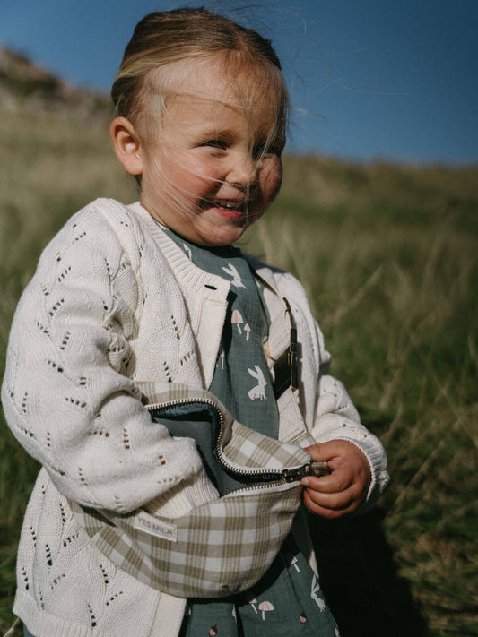 Child holding a checkered bag outdoors with grass and blue sky in the background
