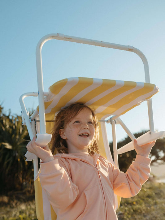Girl holding a beach chair wearing a pink hoodie on a sunny day