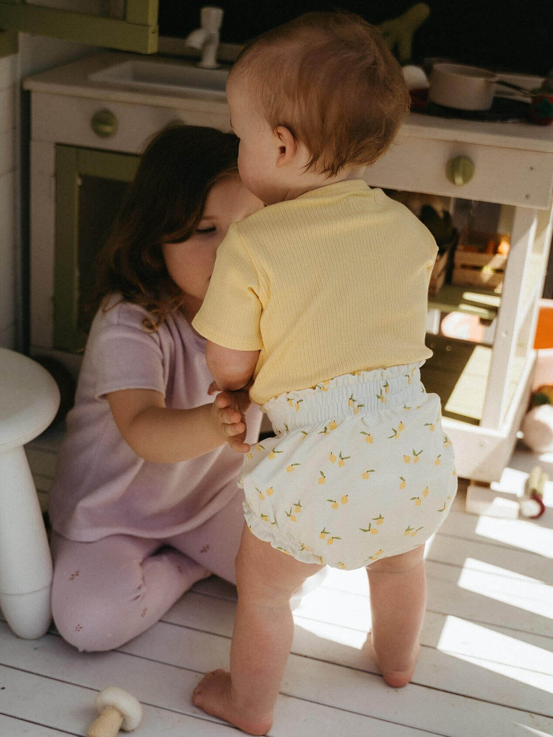 Baby in lemon print bloomers standing at a play kitchen, gifts for 1 year old that get worn