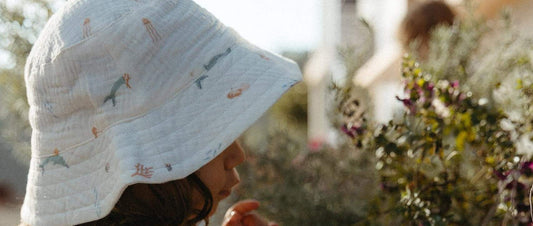 Toddler in a printed muslin bucket hat playing in the garden, an example of sun safe clothing for children
