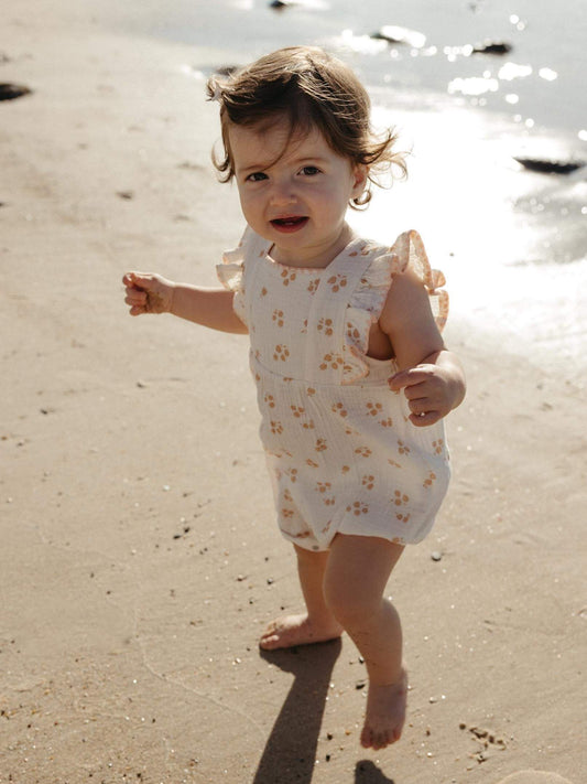Baby girl walking on the sand in a floral organic muslin ruffle romper, a baby girl gift idea for Australian summer