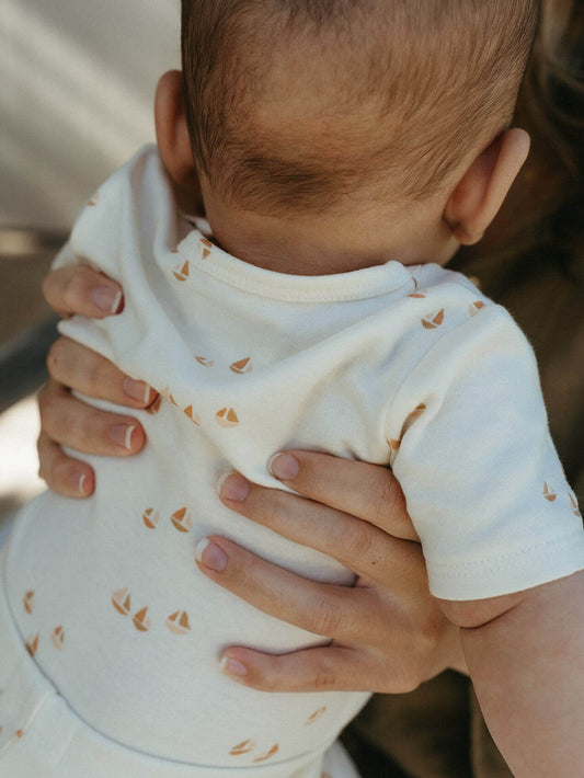 Newborn in a cream sailboat print bodysuit held against a parent's shoulder, a practical baby shower gift
