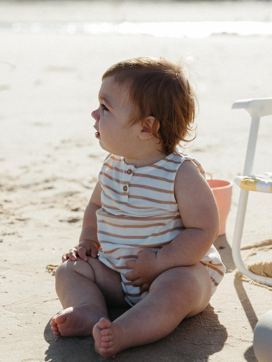 Baby in a sand stripe sleeveless romper sitting on the beach, a first Christmas gift for a newborn in Australia