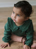 Young child in green long-sleeved top with ruffled collar sitting on wooden floor Baby Ruffle Top - Balsam Baby girl