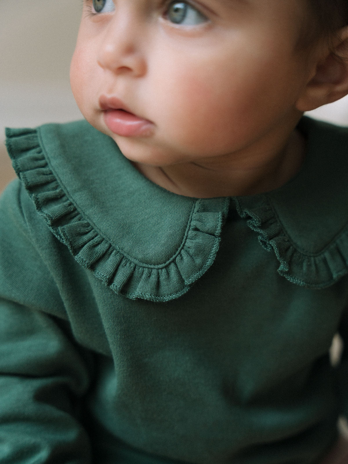Baby wearing a dark green ruffle collar top looking upward Baby Ruffle Top - Balsam Baby girl