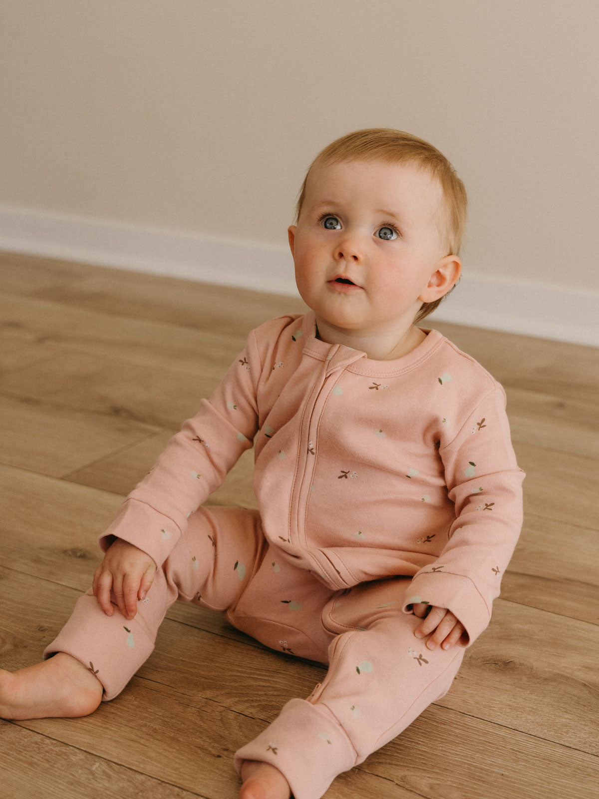 Baby sitting on wooden floor wearing pink printed one-piece pajamas Printed Long Sleeve One Piece - Autumn Harvest Rosehip Baby girl
