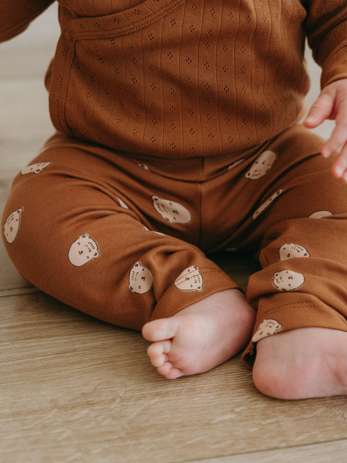 Baby wearing rust-colored sweater and bear-printed leggings sitting on wooden floor Baby Printed Leggings - Cosy Bear Russet Baby boy