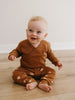 Baby sitting on wooden floor wearing brown textured top and patterned pants Baby Printed Leggings - Cosy Bear Russet Baby boy