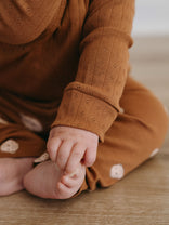 Baby in rust-colored pointelle bodysuit sitting on wooden floor Pointelle Crossover Bodysuit - Russet Baby boy
