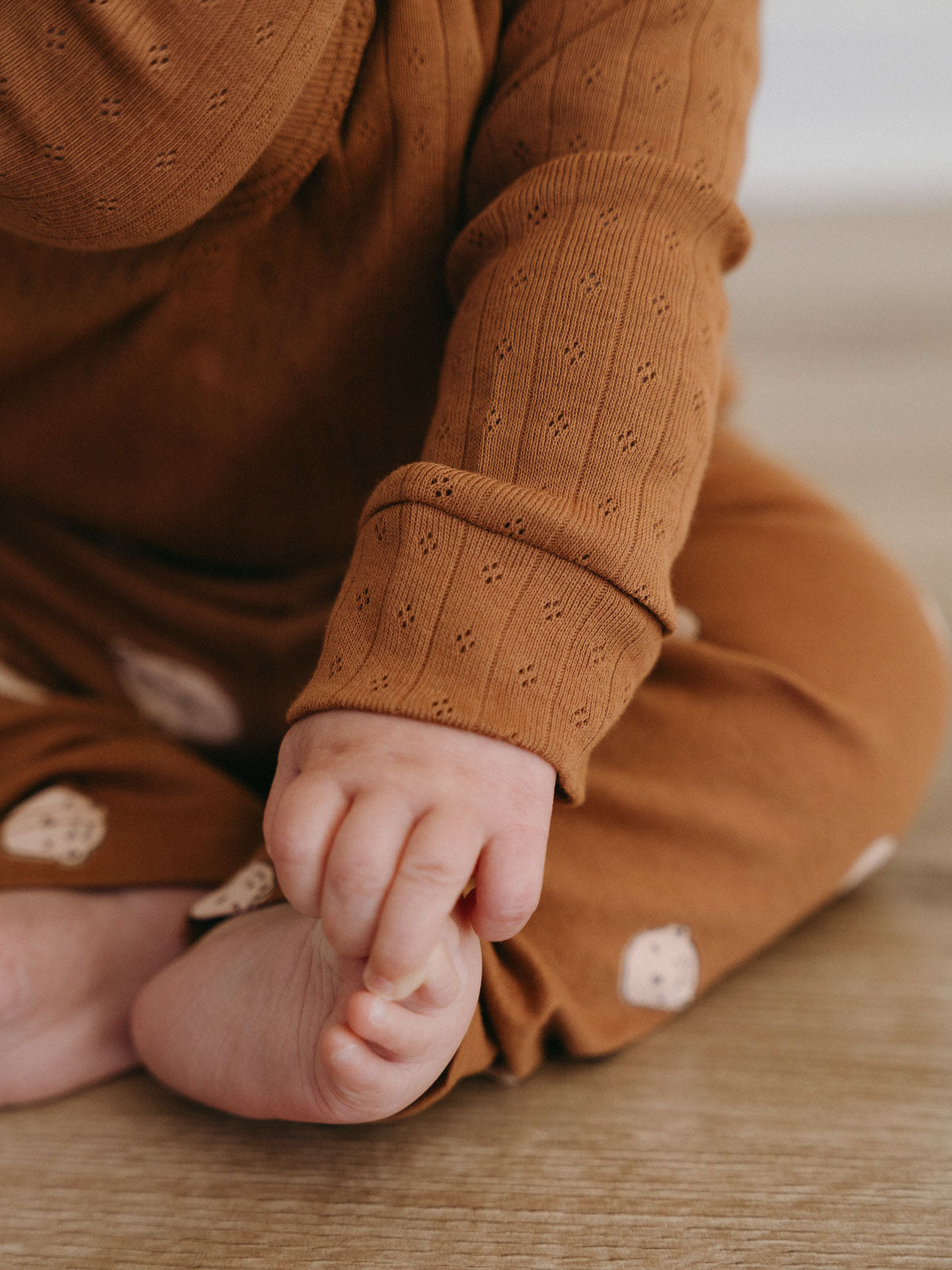 Baby in rust-colored pointelle bodysuit sitting on wooden floor Pointelle Crossover Bodysuit - Russet Baby boy