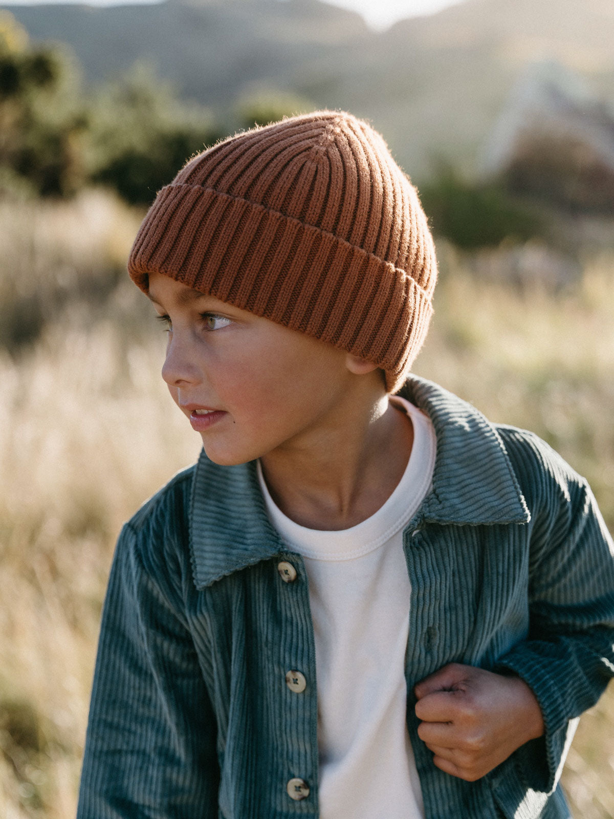 Young boy wearing a brown ribbed beanie and green corduroy jacket outdoors Ribbed Beanie - Russet Girls and Boys