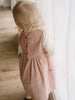 Child wearing a pink corduroy dress standing indoors with a neutral background