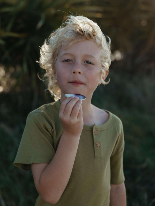 Boy holding a shell at the beach wearing a green tee
