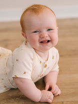 Baby with red hair smiling on wooden floor wearing patterned short sleeve bodysuit Henley Short Sleeve Bodysuit - Autumn Harvest Ecru Baby girl