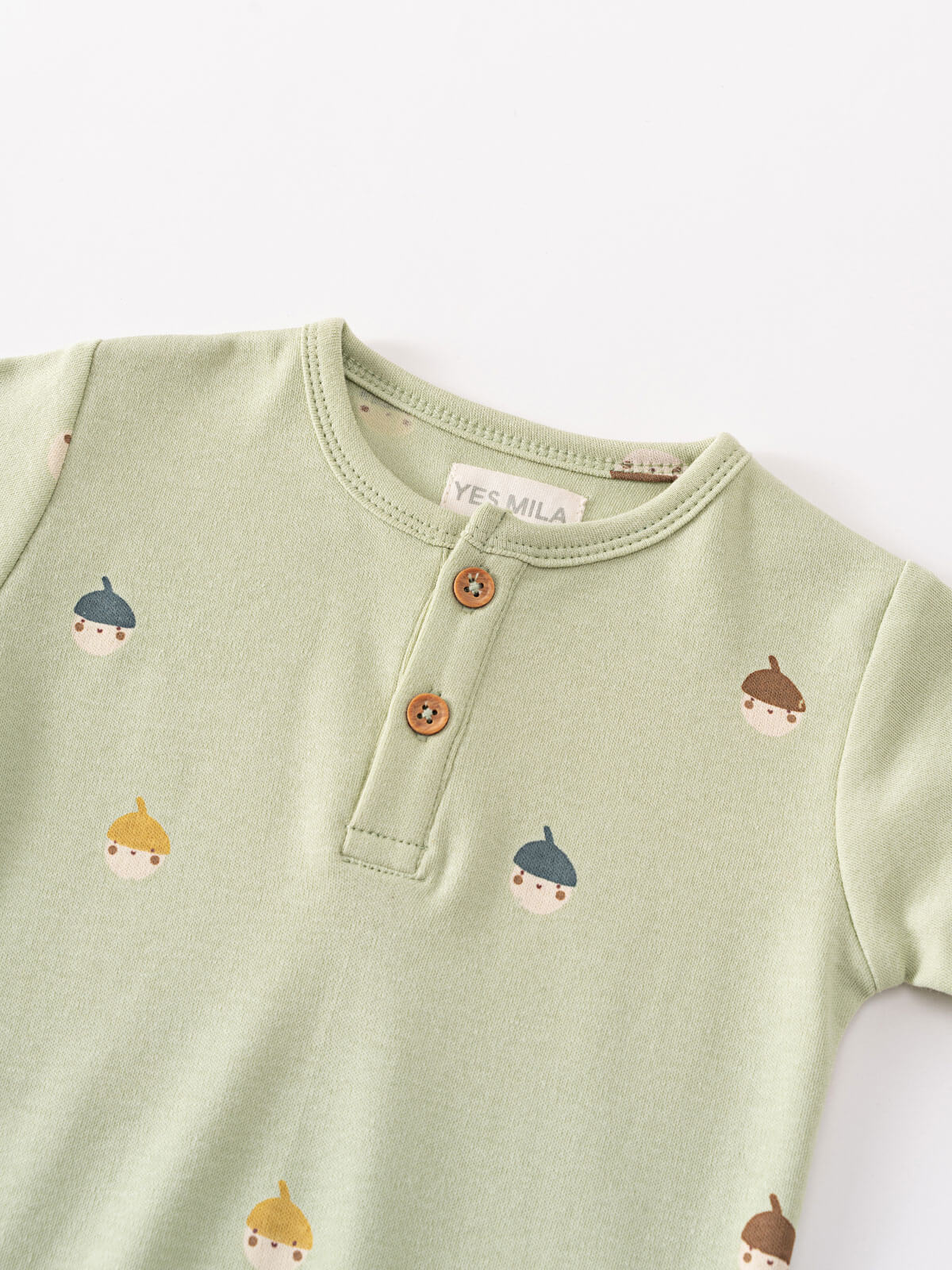 Close-up of a sage green baby bodysuit with acorn face pattern and button placket Henley Short Sleeve Bodysuit - Little Acorn Sage Baby boy