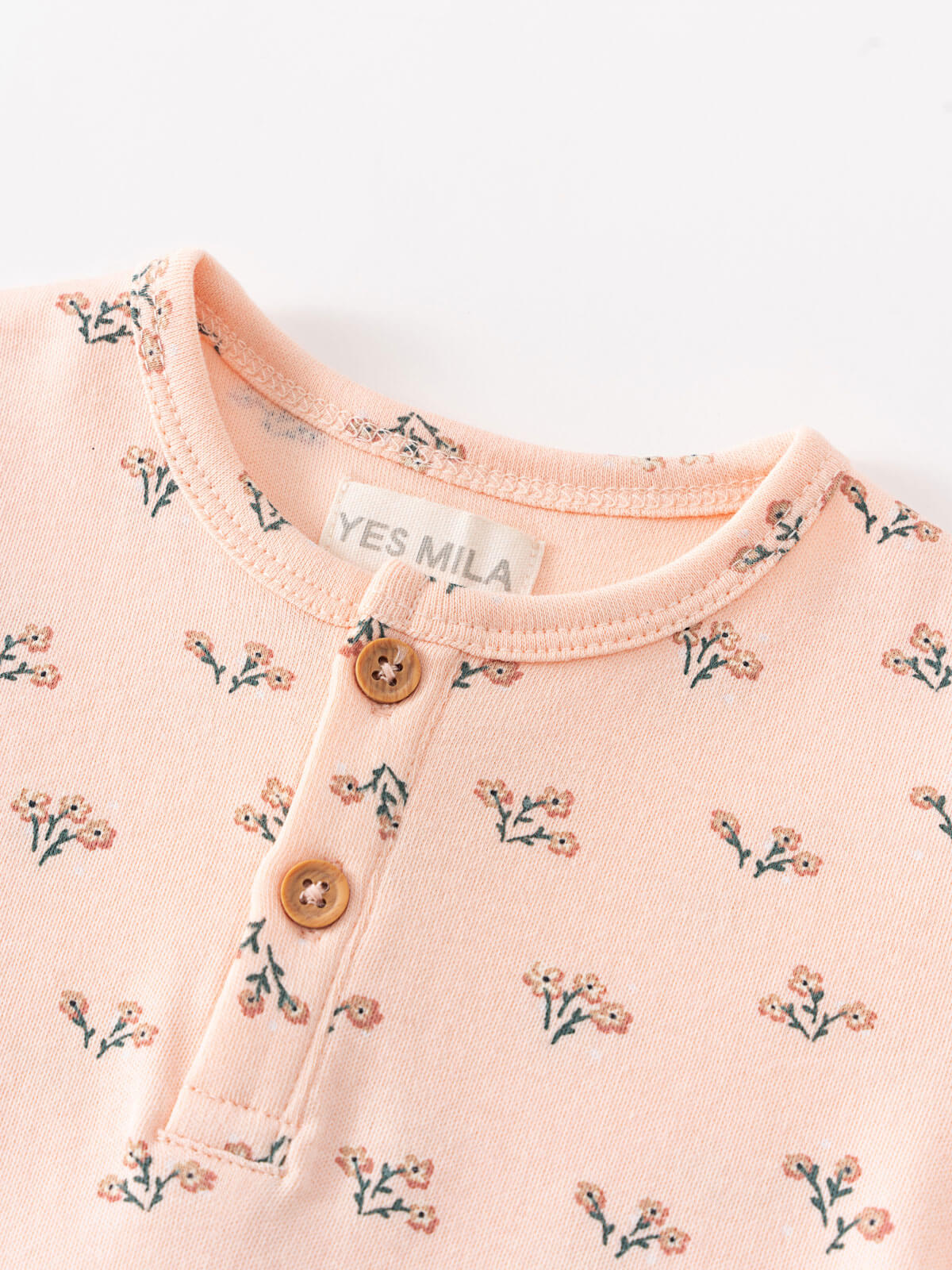 Close-up of a peach bodysuit with small floral print and wooden buttons Henley Short Sleeve Bodysuit - Wildflower Bouquet Pink Baby girl