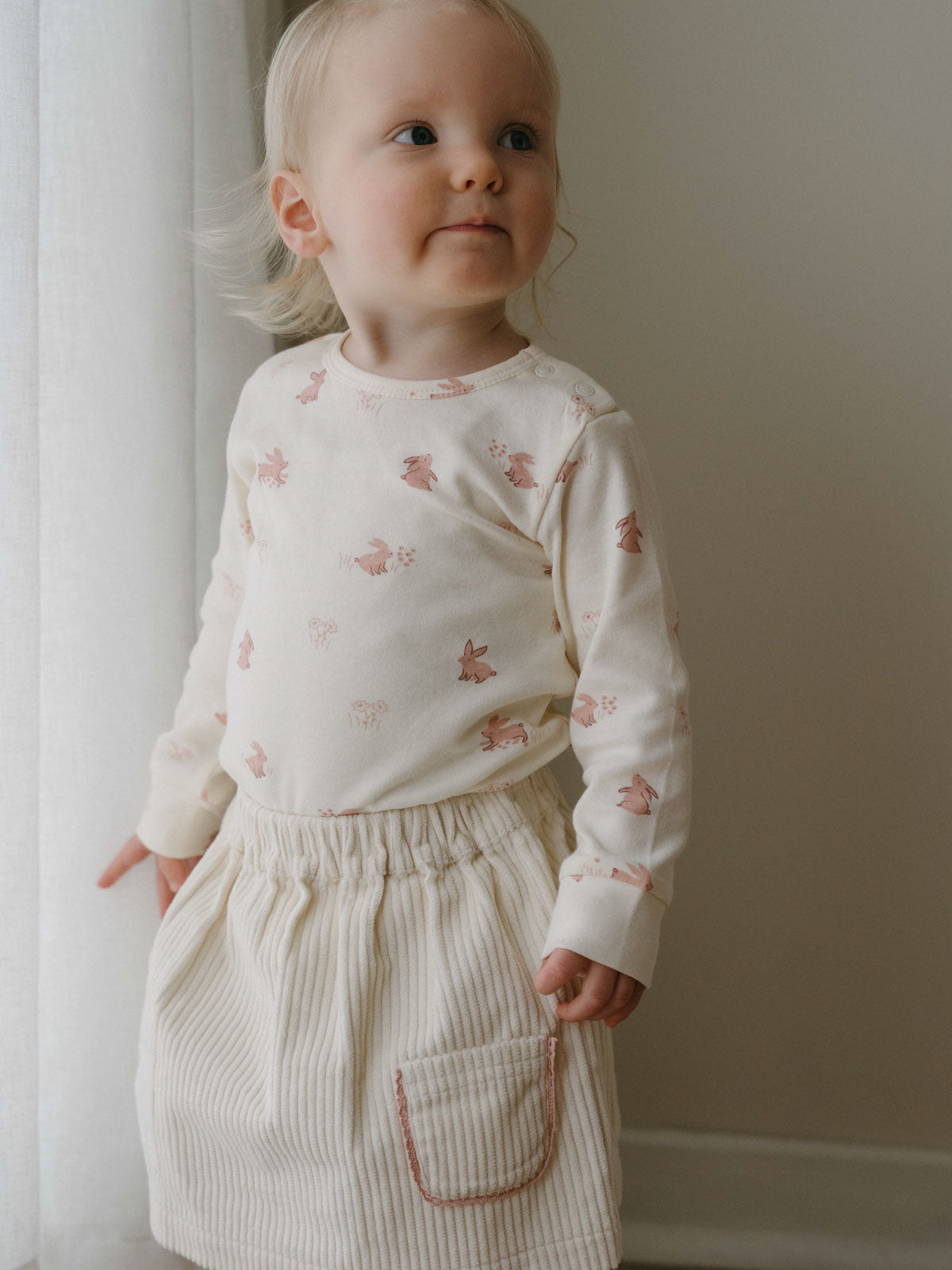 Toddler in a patterned long sleeve top and corduroy skirt standing indoors Long Sleeve Bodysuit - Meadow Friends Ecru Baby girl