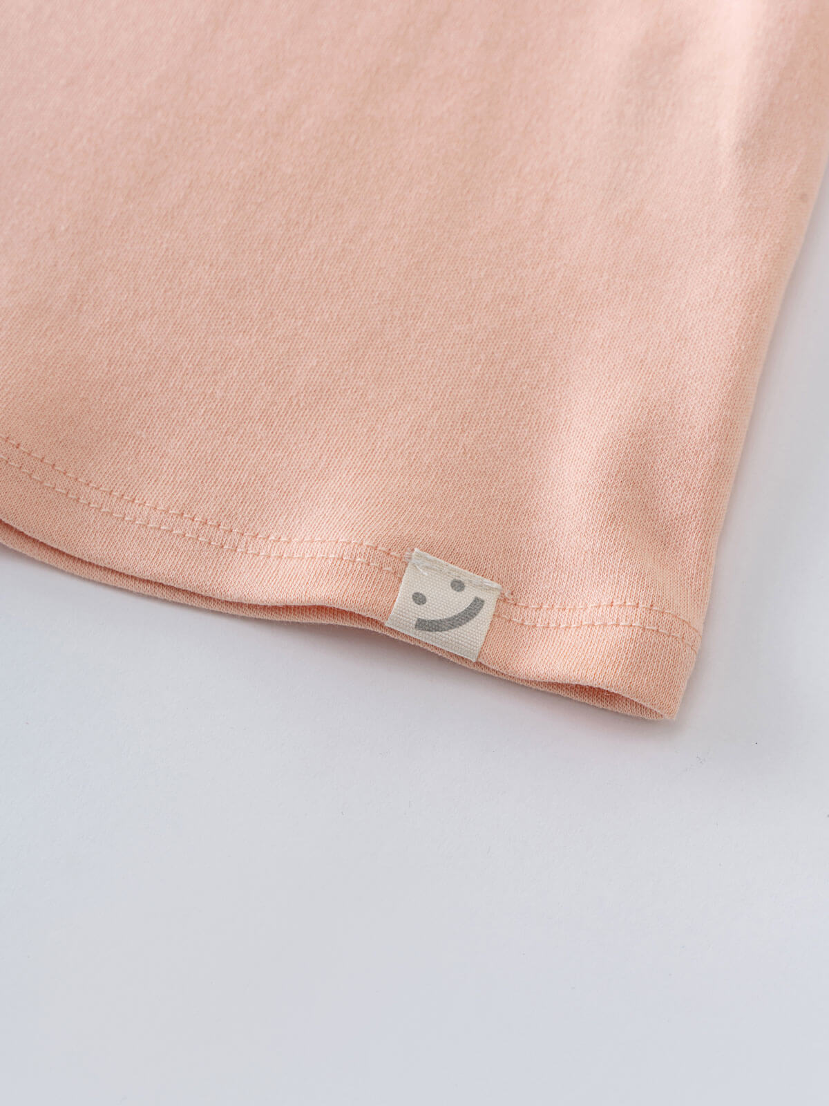 Close-up of peach fabric hem with small smiley face label tag Long Sleeve Jersey Dress - Mallow Girls