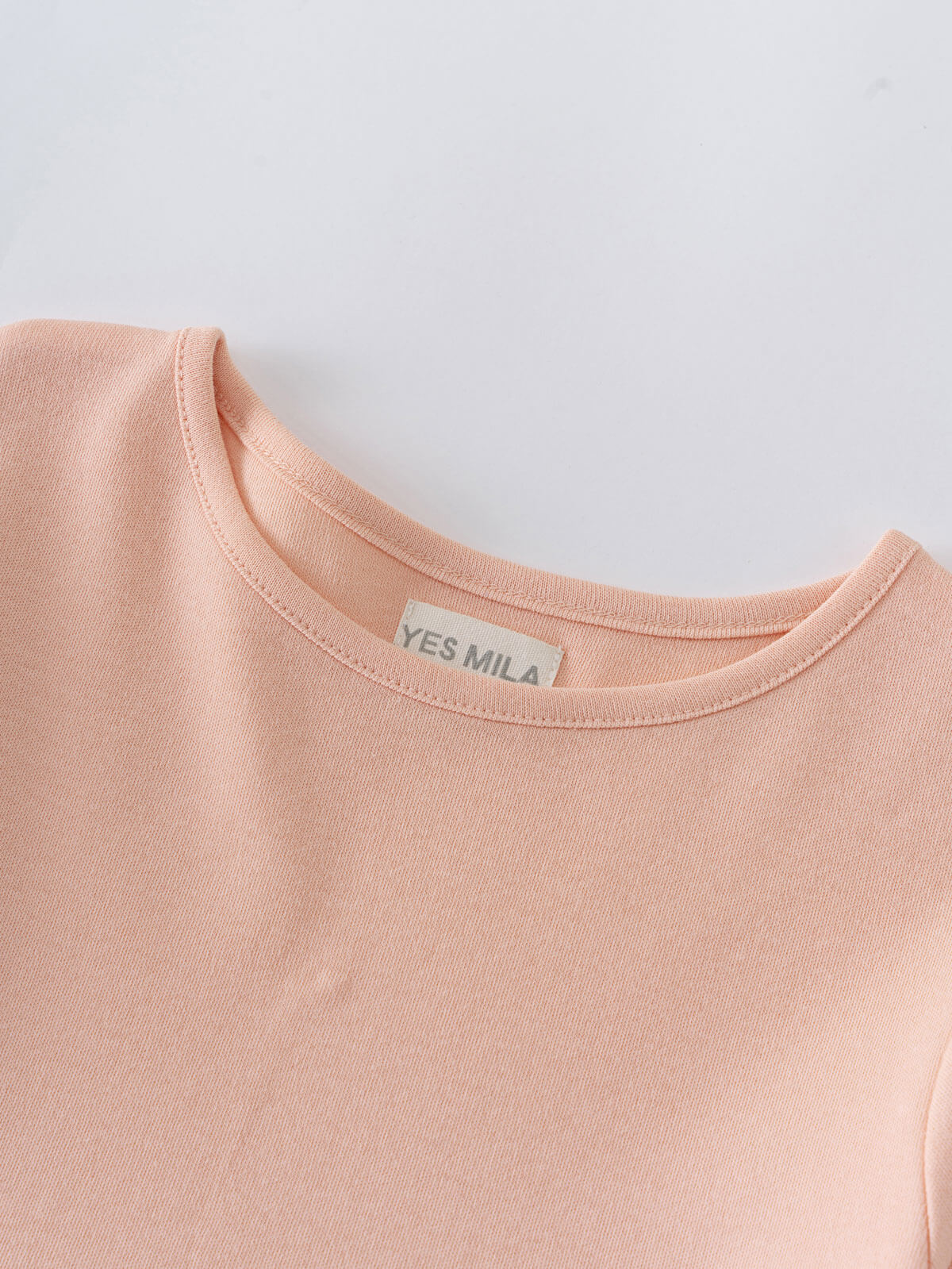 Close-up of a peach-colored jersey garment neckline with a white label Long Sleeve Jersey Dress - Mallow Girls