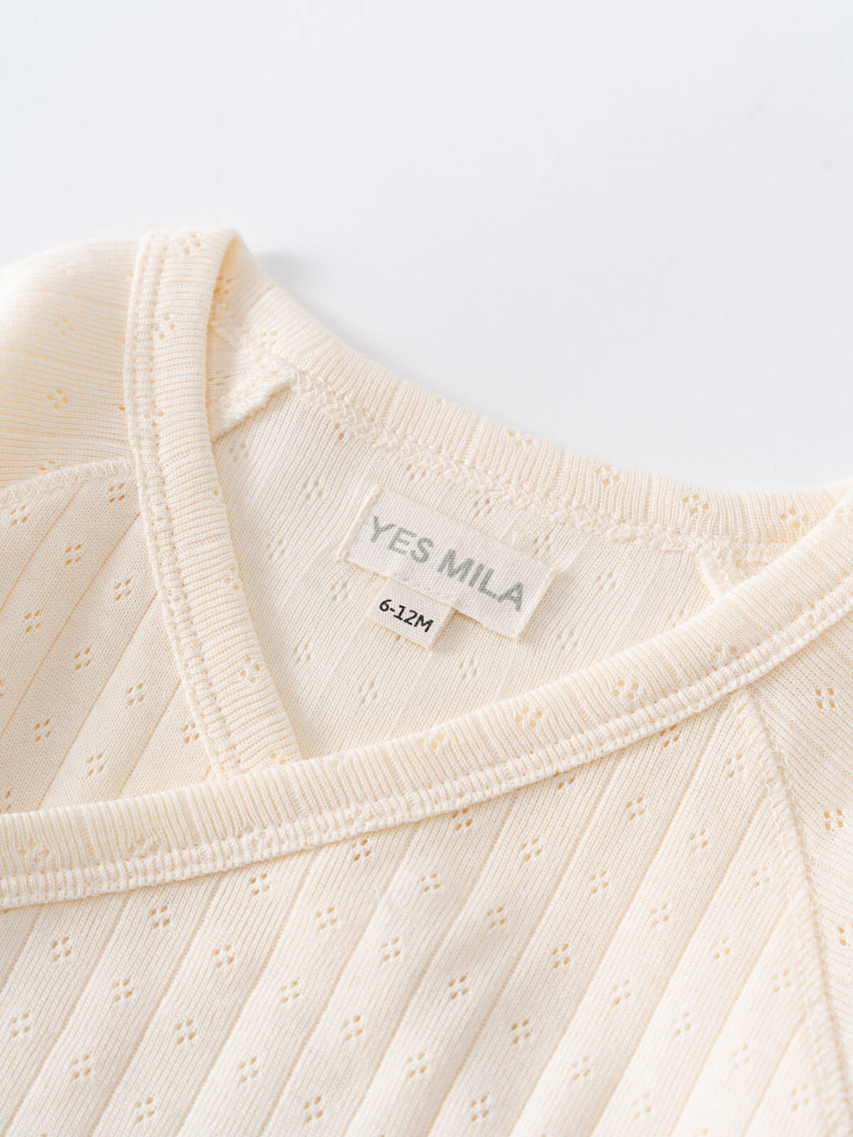 Close-up of cream-colored pointelle fabric bodysuit showing size label and neckline detail Pointelle Crossover Bodysuit - Ecru Baby boy