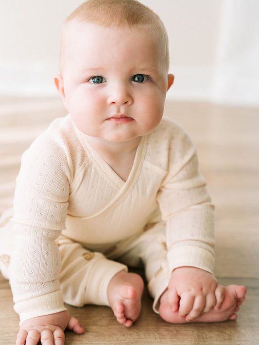 Baby wearing a cream crossover bodysuit sitting on a wooden floor Pointelle Crossover Bodysuit - Ecru Baby boy