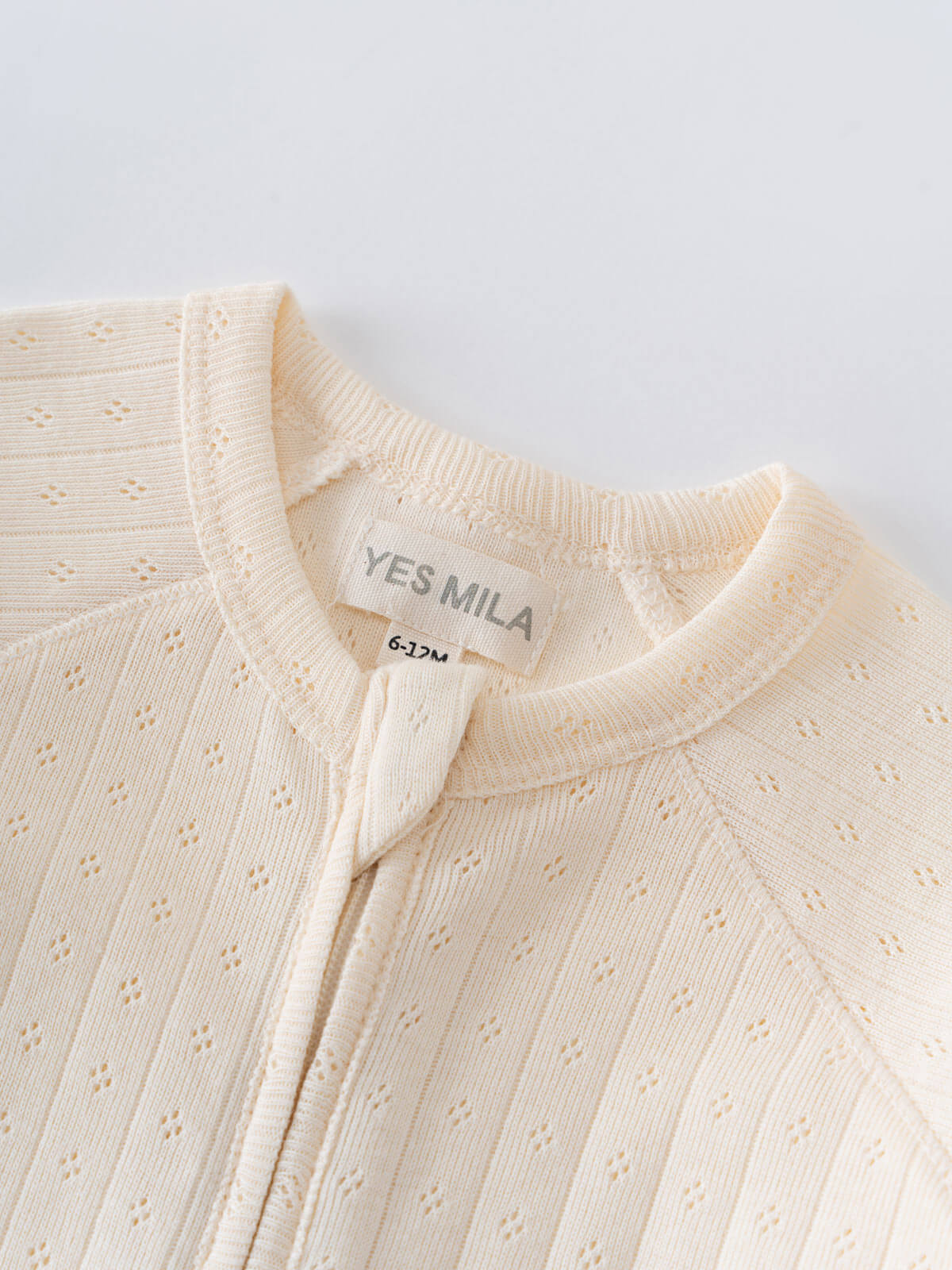 Close-up of a cream-colored sweater with 'YES MILA' label on a light gray background Pointelle Long Sleeve One Piece - Ecru Baby boy