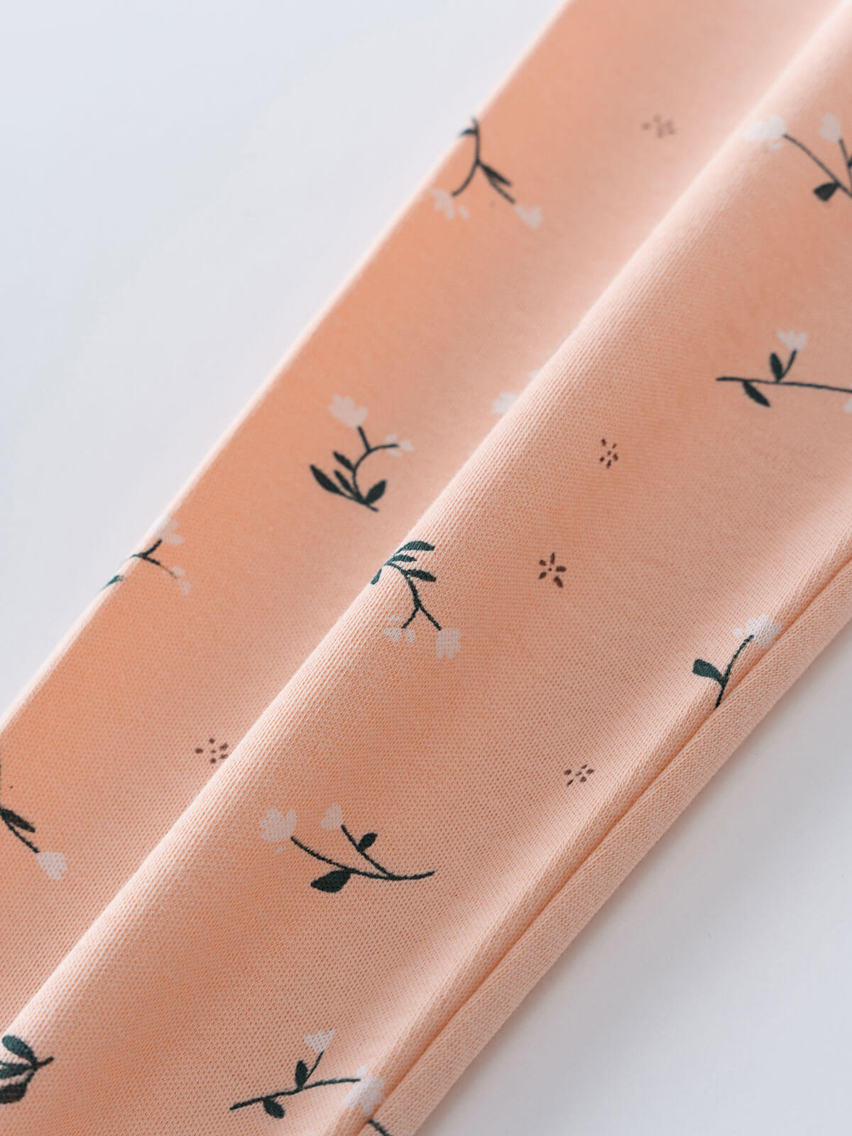 Close-up of peach fabric with small dark green plant and floral pattern Printed Leggings - Wild Meadow Mallow Girls
