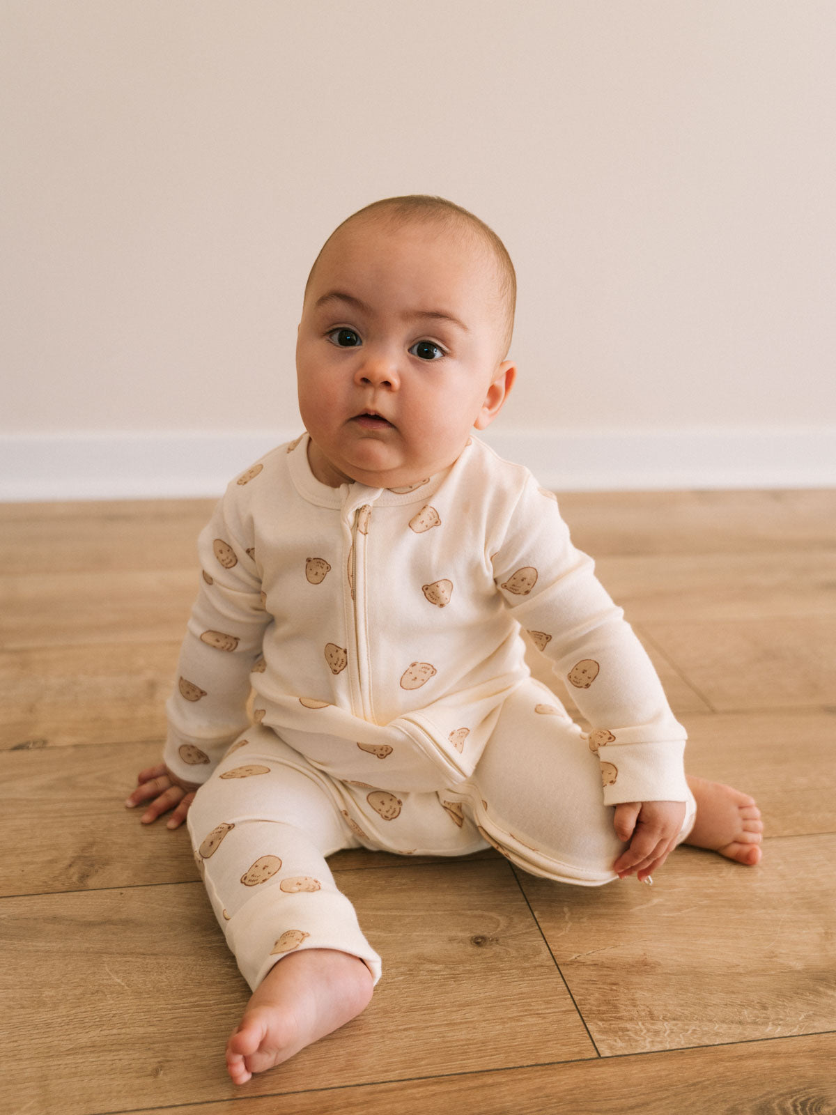 Baby sitting on wooden floor wearing cream pajamas with bear print Printed Long Sleeve One Piece - Cosy Bear Ecru Baby boy