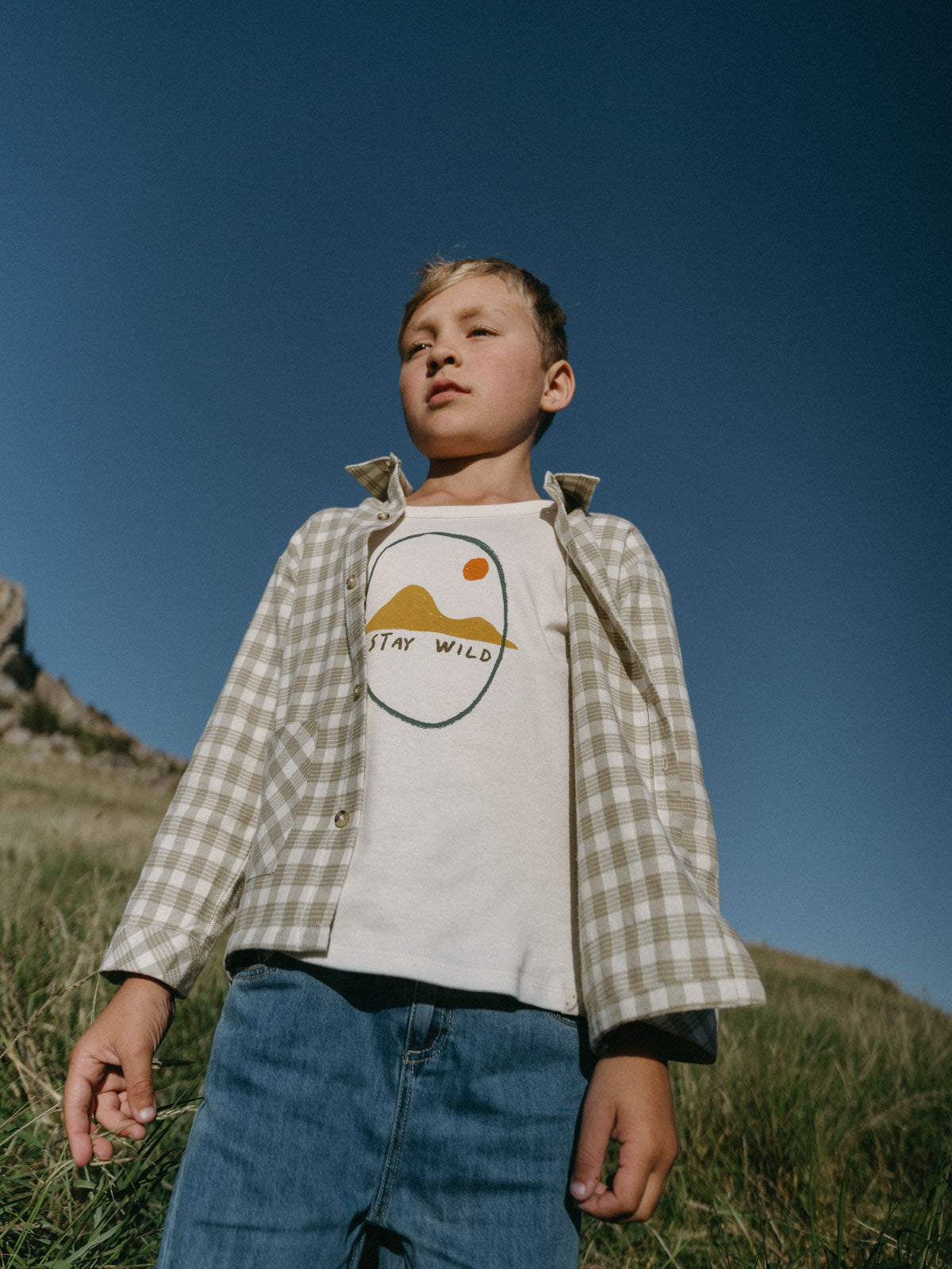 Young boy wearing graphic tee and plaid shirt standing outdoors on grass Printed Long Sleeve Tee - Stay Wild Boys