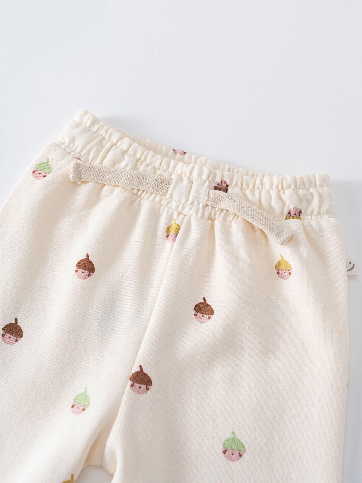 Close-up of cream-colored pants with small acorn face print pattern Printed Sweatpants - Little Acorn Ecru Baby girl