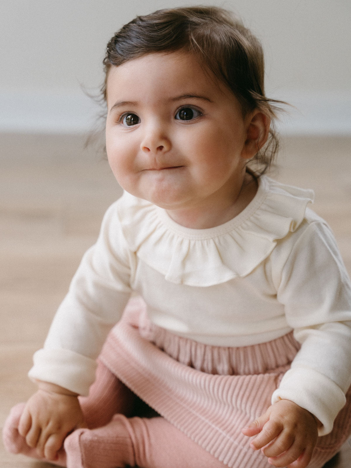 Baby girl sitting on the floor wearing a white ruffled collar bodysuit Ruffle Long Sleeve Bodysuit - Ecru Baby girl