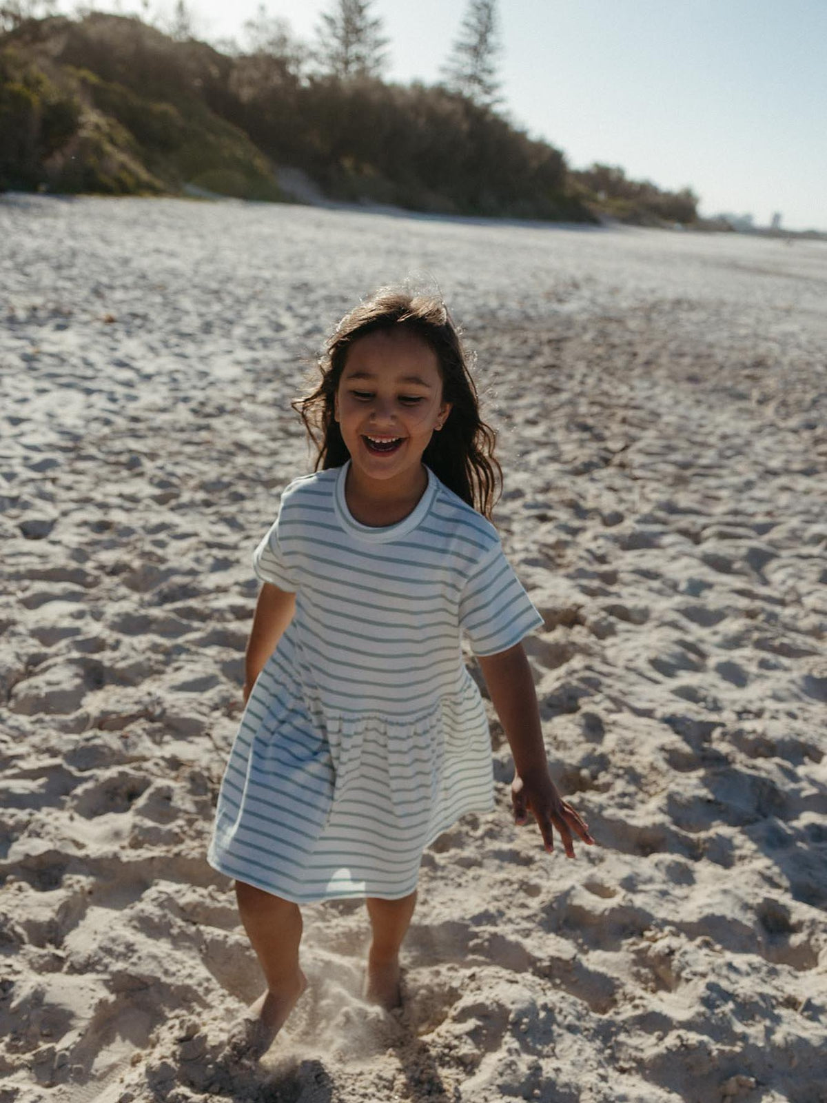Girl walking on the beach wearing a green and white striped dress