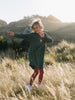 Young girl jumping in a grassy field wearing a green sweatshirt dress Sweatshirt Dress - Dove Girls