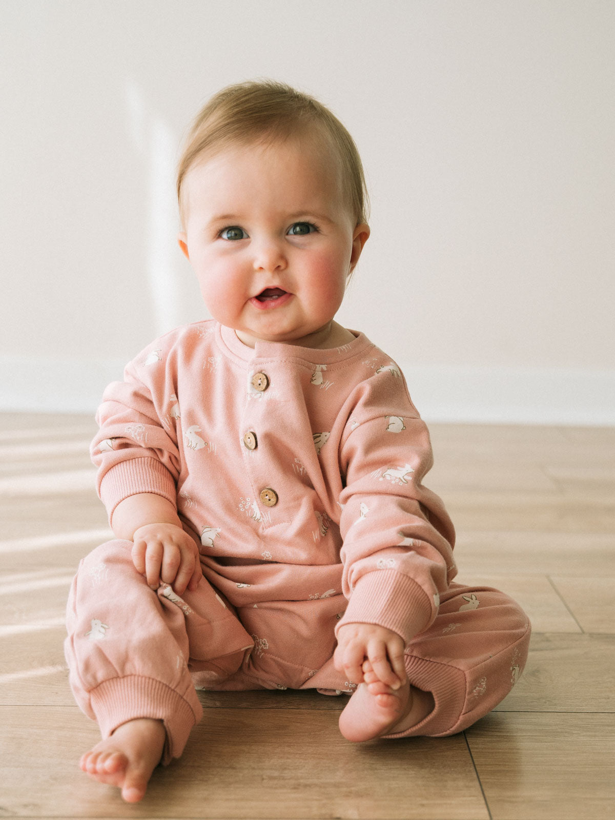 Baby sitting on wooden floor wearing pink patterned sweatshirt and pants outfit Sweatshirt Onesie - Meadow Friends Blush Baby girl