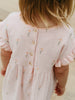 Close-up of a child wearing a pink dress with floral embroidery on a neutral background Amara Dress - Poppy Field Girls