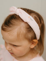 Child wearing a pink headband with a subtle design on a plain background