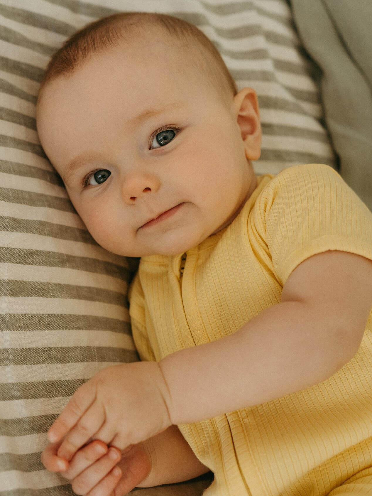 Baby in a yellow outfit lying on a striped surface