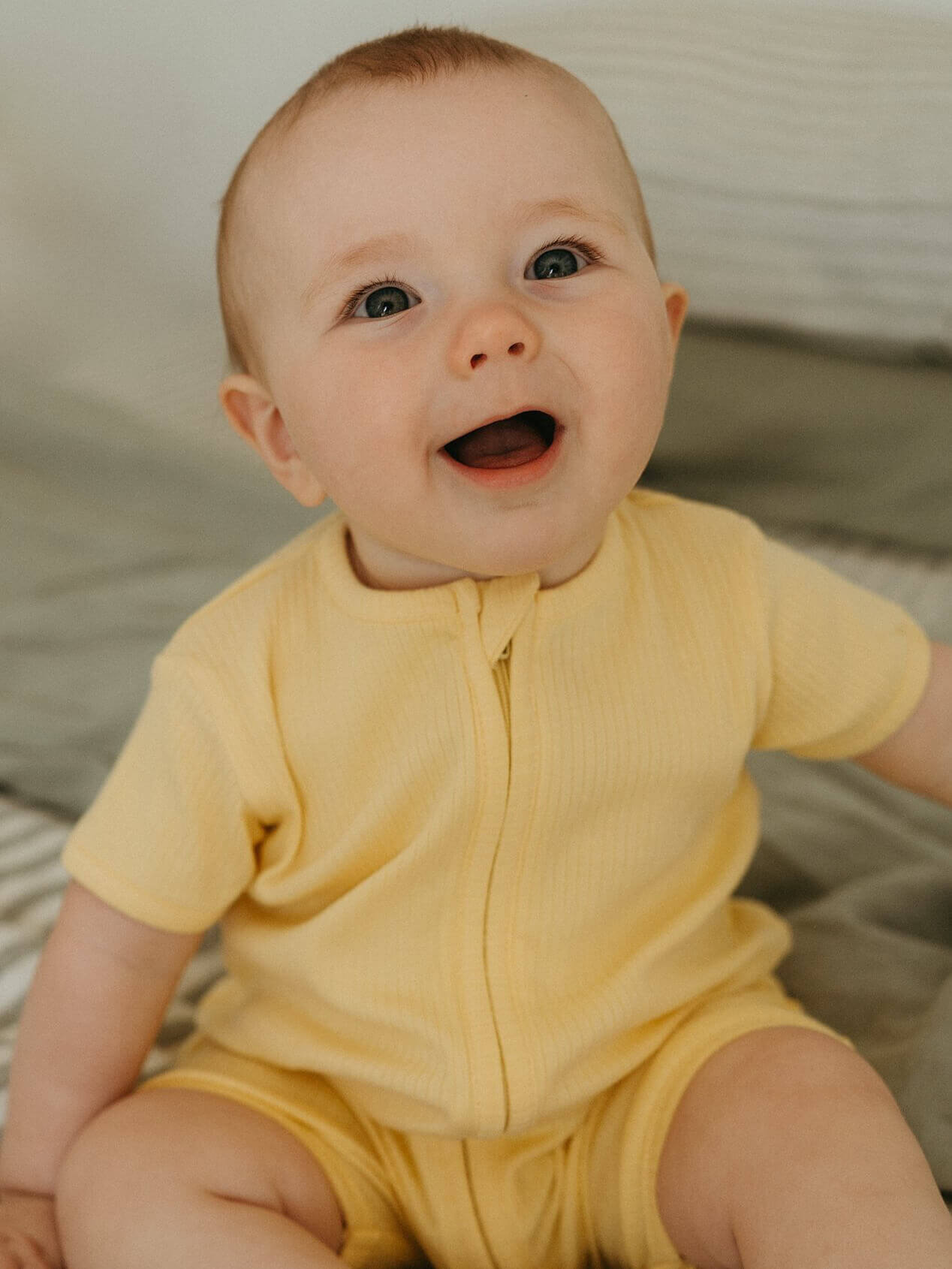 Baby wearing a yellow outfit sitting on a soft surface